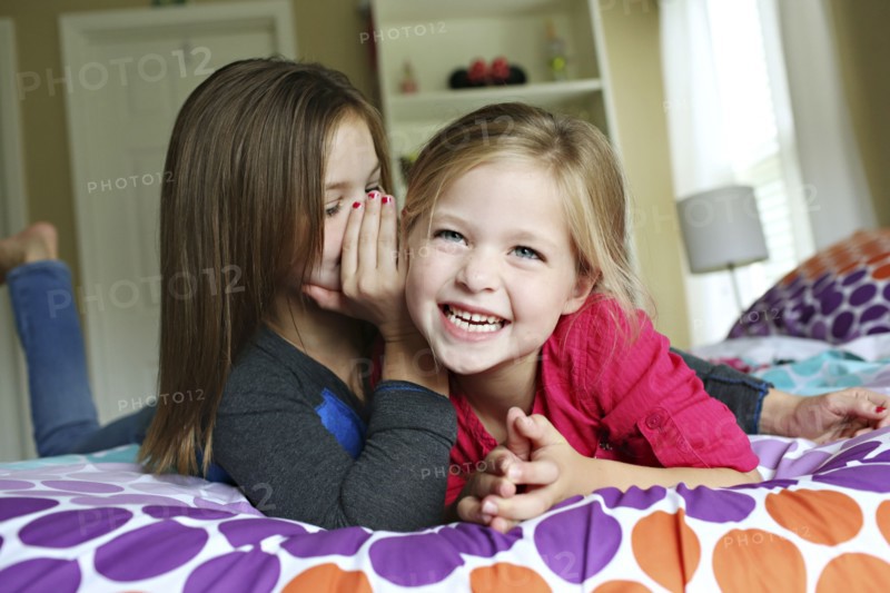 Close up of sisters whispering on bed