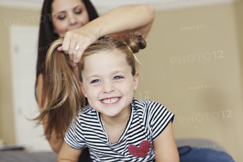 Mother styling hair of daughter on bed