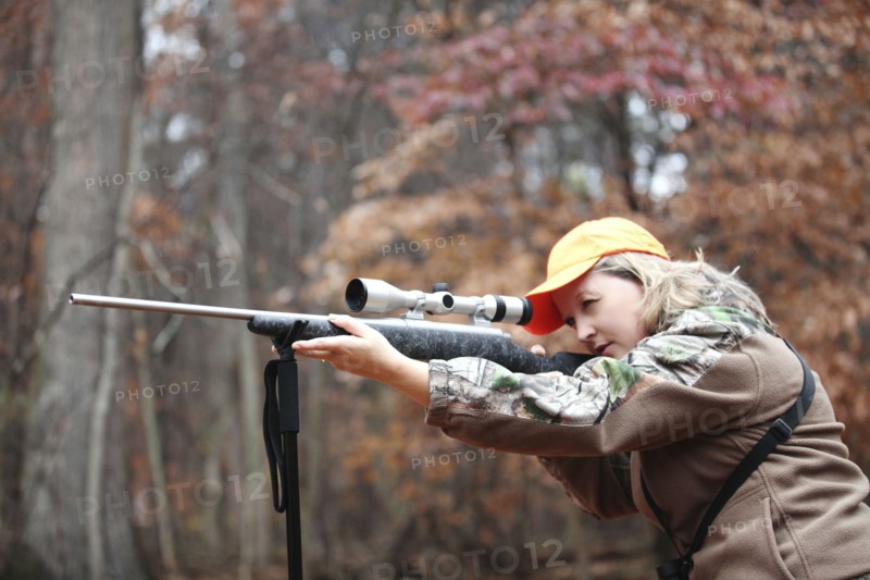 Hunter in camouflage aiming rifle in forest