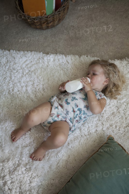 High angle view of preschooler girl drinking bottle on rug