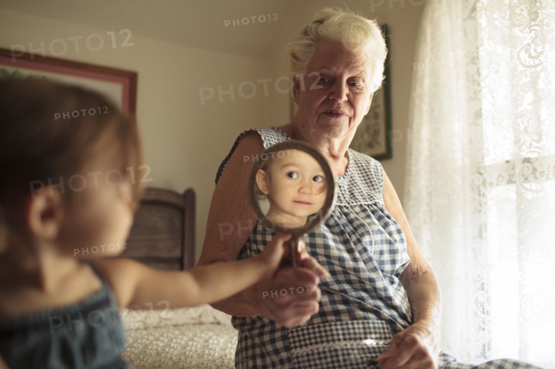 Grandmother holding mirror for granddaughter on bed