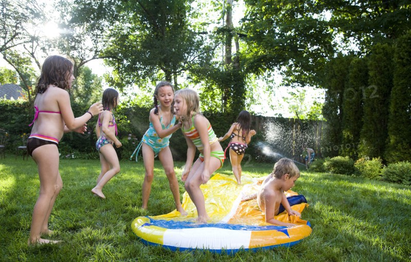 Children playing on water slide in backyard
