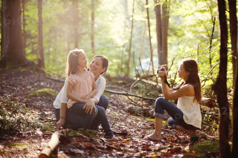 Caucasian girl photographing mother and sister in forest