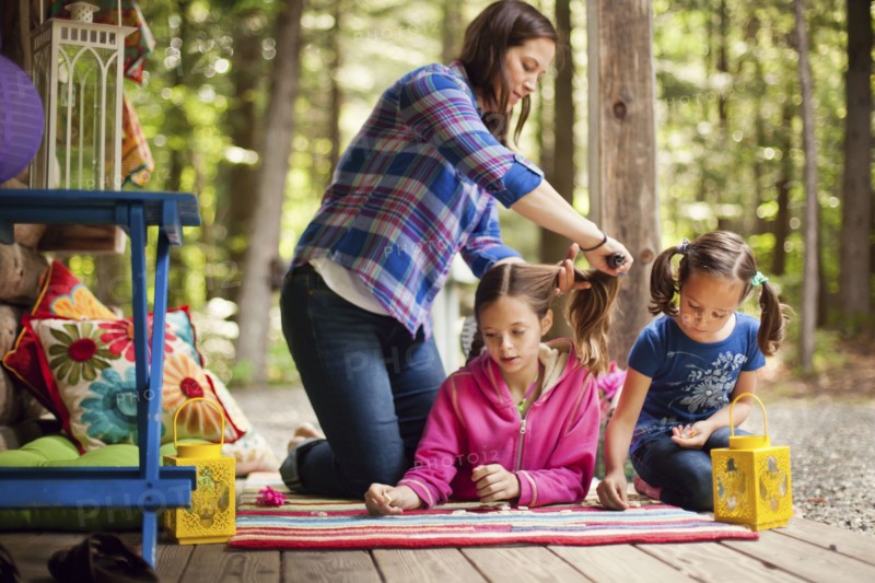Caucasian mother brushing hair of daughter on porch
