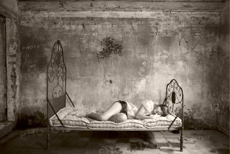 Caucasian woman laying on bed in dilapidated room