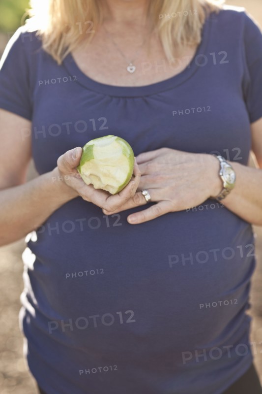 Pregnant Caucasian woman eating apple outdoors