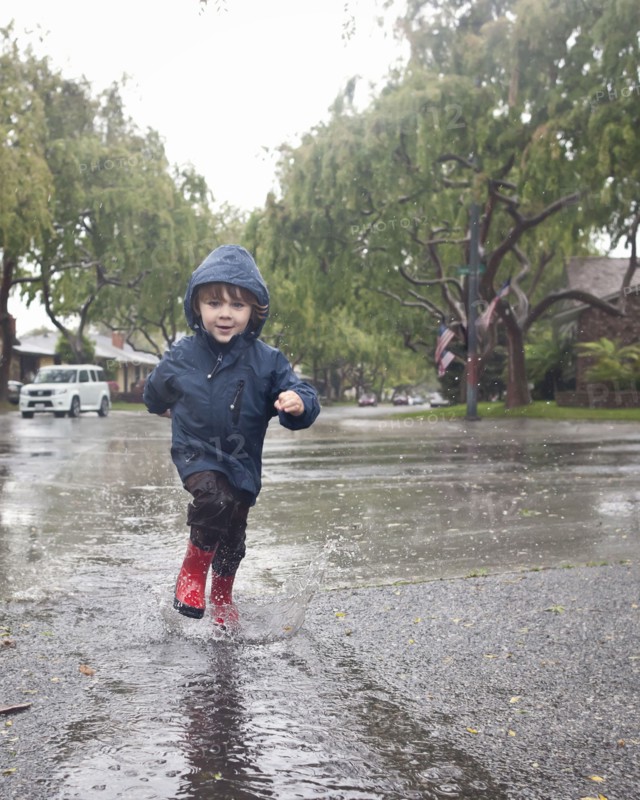 Caucasian boy splashing in rain puddle