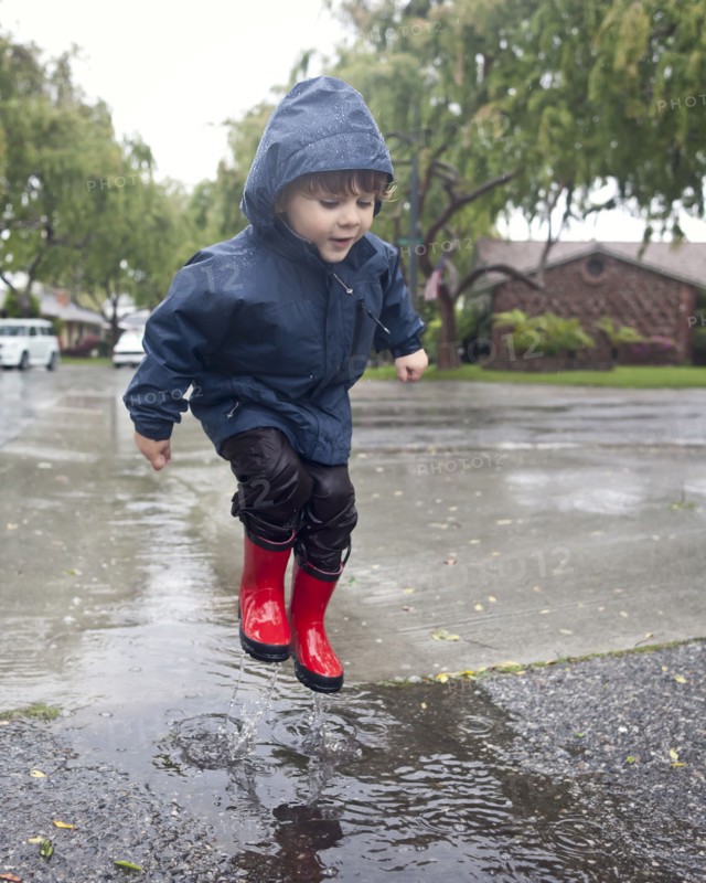 Caucasian boy jumping in rain puddle