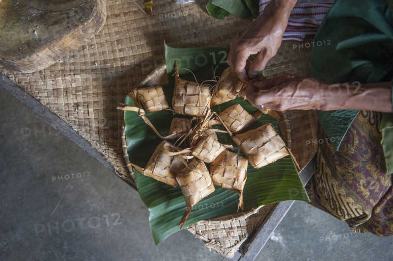 Asian man knotting woven packages on floor