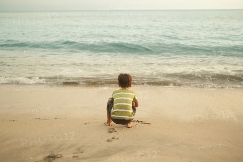 Mixed race boy squatting on beach playing