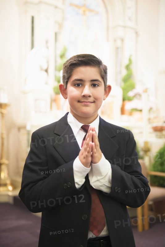 Hispanic boy with hands clasped in church