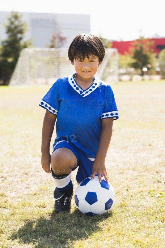 Hispanic boy with soccer ball kneeling on field