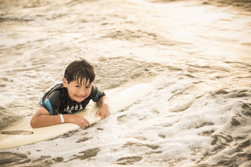 Hispanic boy floating on surfboard in ocean