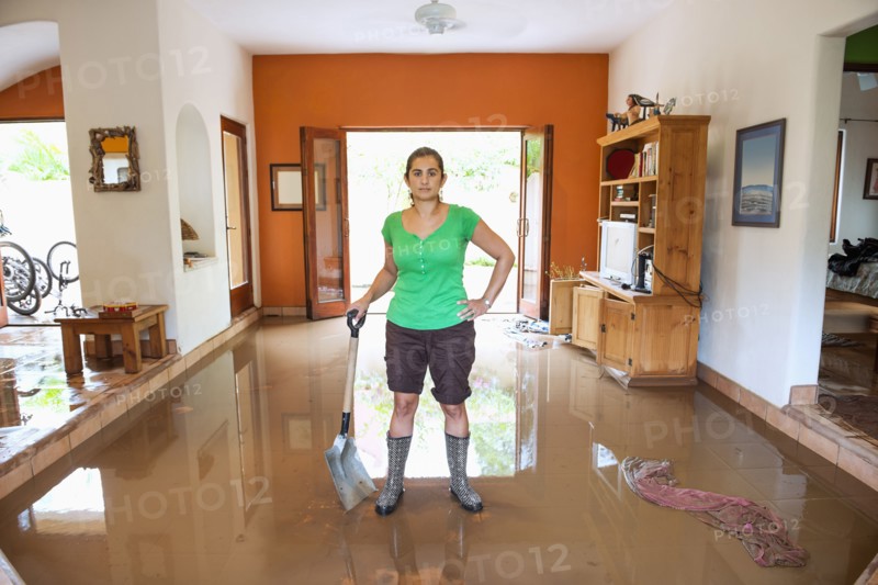 Hispanic woman shoveling water out of flooded house