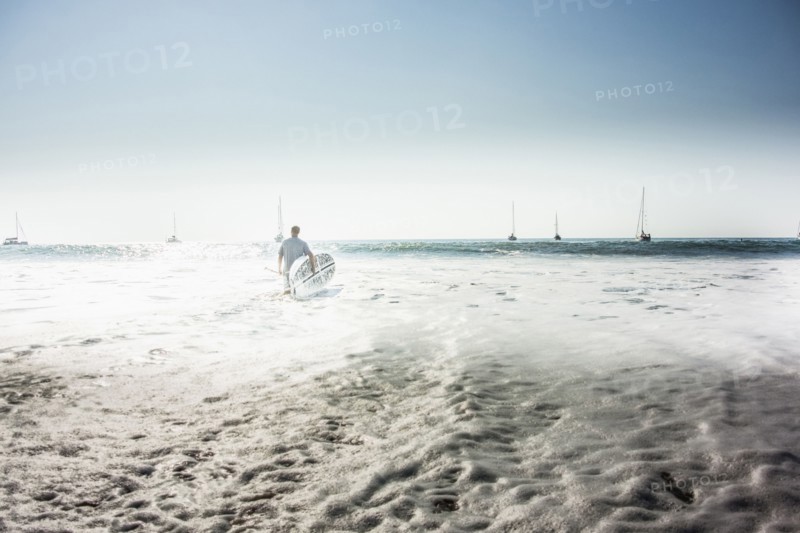 Caucasian man carrying surfboard into ocean