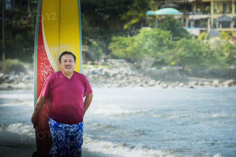 Older Hispanic man with surfboard on beach