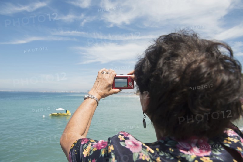 Older woman taking photograph of tropical ocean