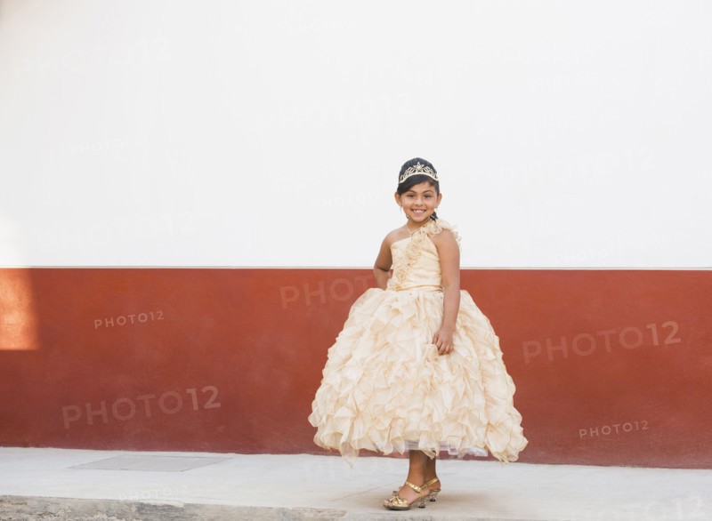 Hispanic girl posing in ornate gown and tiara