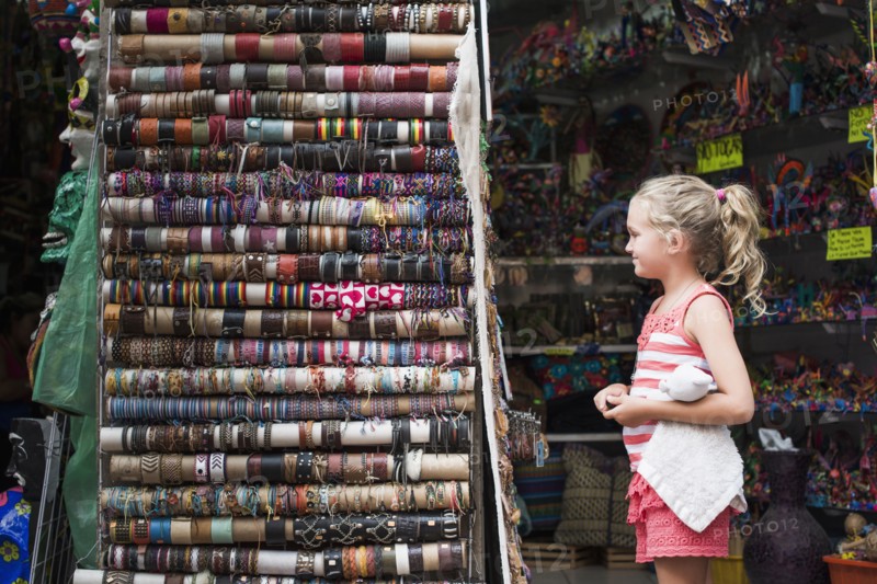 Caucasian girl admiring woven bracelets for sale in market