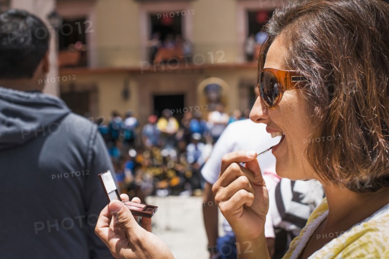 Close up of Hispanic woman applying makeup in mirror outdoors