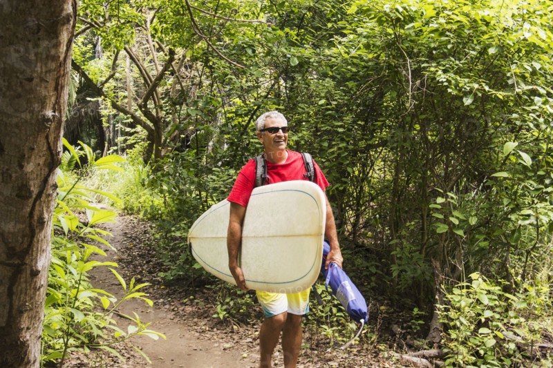 Caucasian man carrying surfboard in jungle