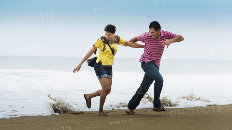 Hispanic couple playing near waves on beach