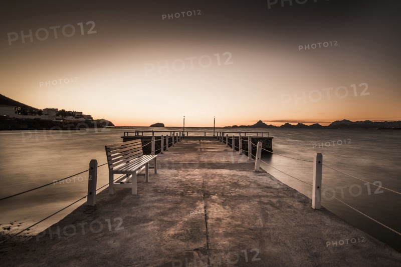 Stone walkway and ocean waves under sunset sky