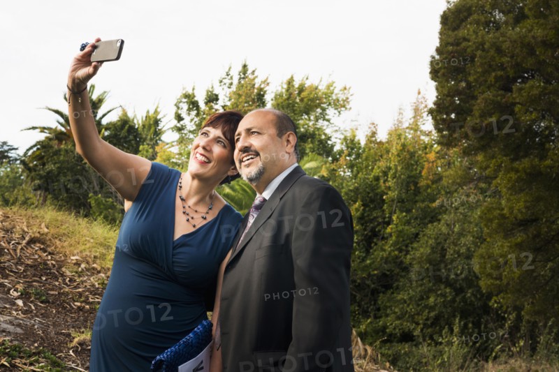 Hispanic couple taking cell phone selfie in formal wear