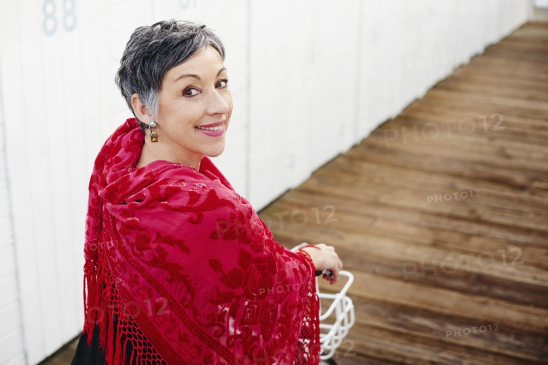Older Caucasian woman with red shawl riding bicycle