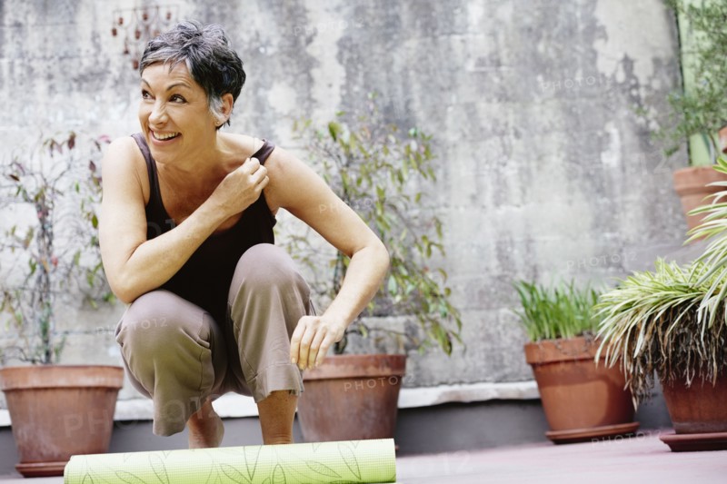 Older Caucasian woman rolling up yoga mat in courtyard