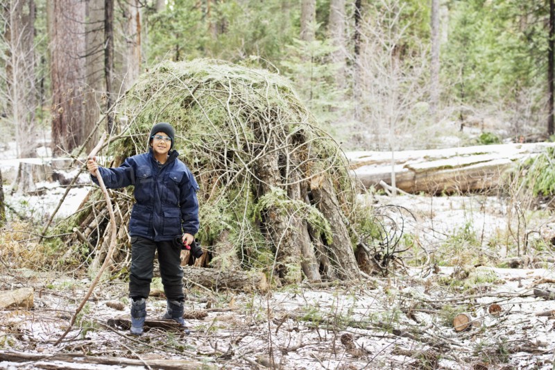 Hispanic boy building hut from branches in forest