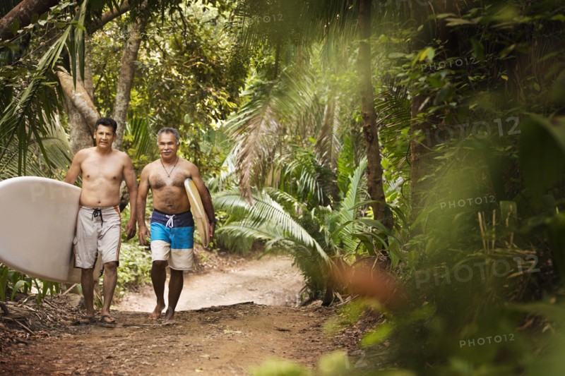 Hispanic men carrying surfboards on jungle trail