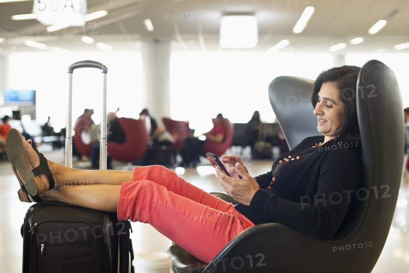 Hispanic businesswoman using cell phone in airport waiting area