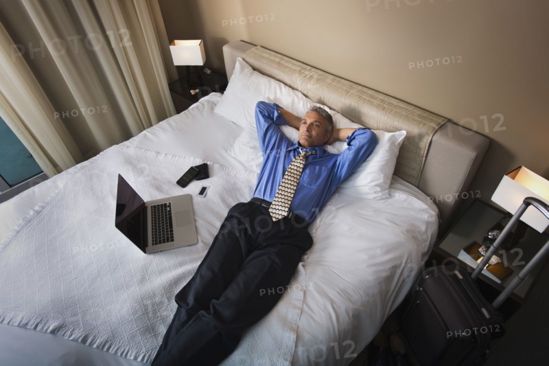 Caucasian businessman laying with laptop on hotel bed