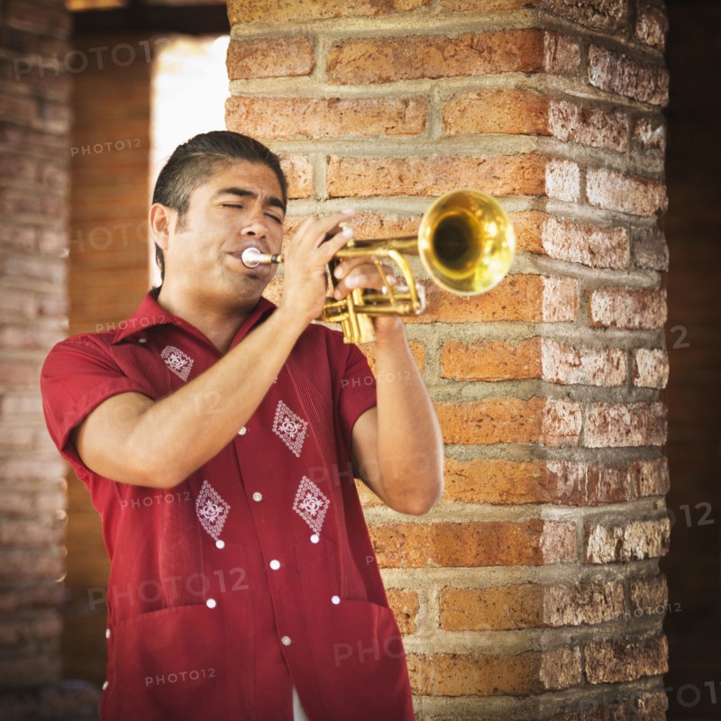 Hispanic musicians playing trumpet near brick wall