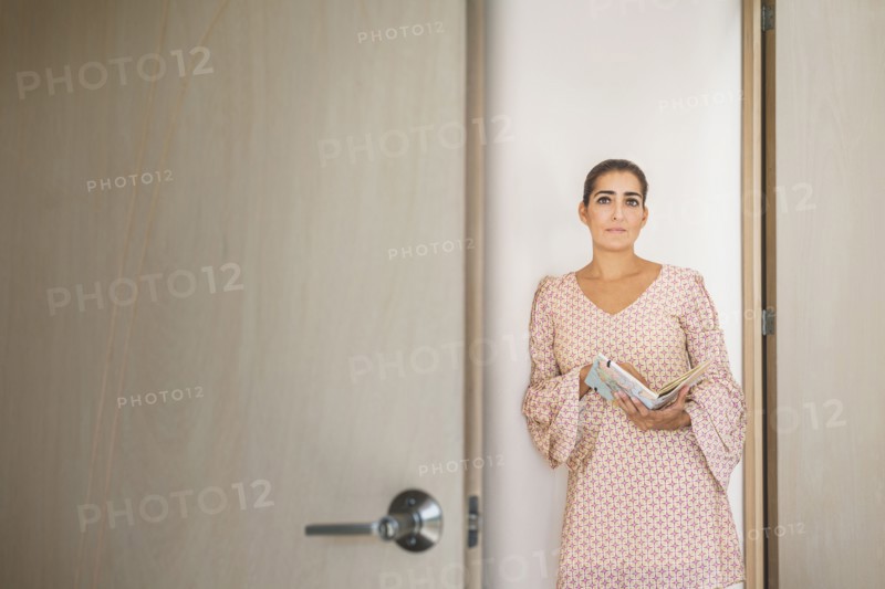 Worried Hispanic woman peering through door crack