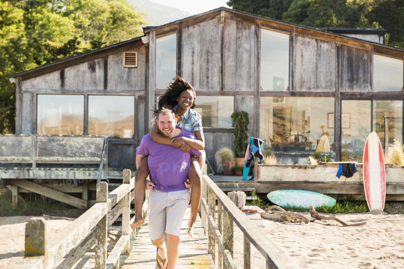 Man carrying girlfriend piggyback on wooden deck