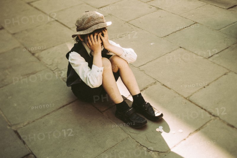 Old-fashioned Caucasian sitting in street crying