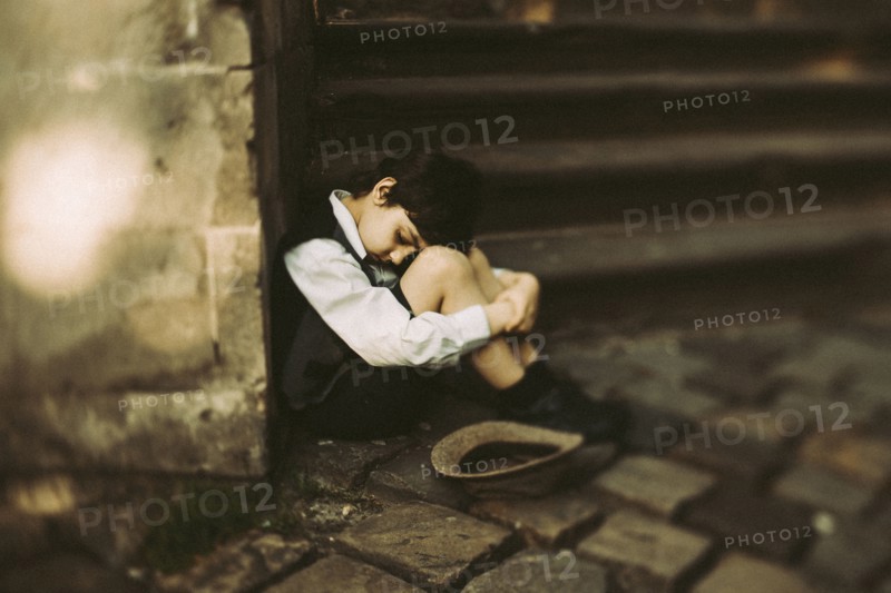 Old-fashioned Caucasian boy sitting near staircase begging for money