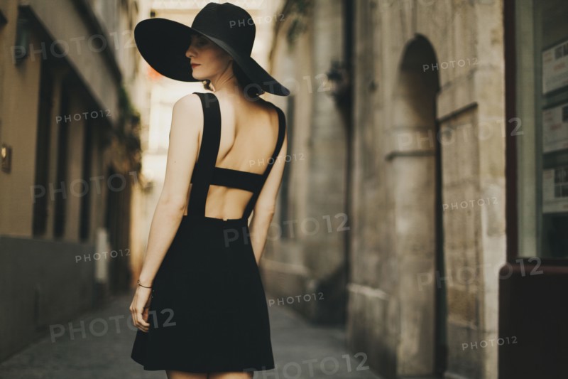 Caucasian woman wearing black dress and sun hat in street