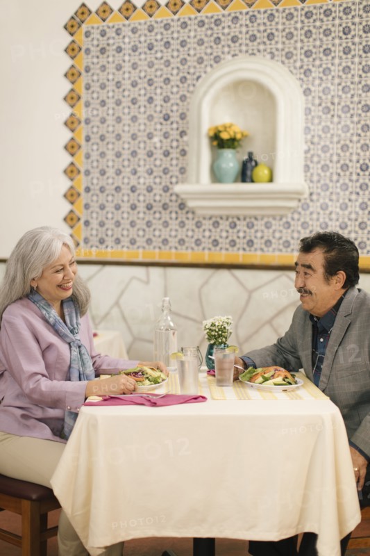 Smiling older couple eating salad and laughing in restaurant