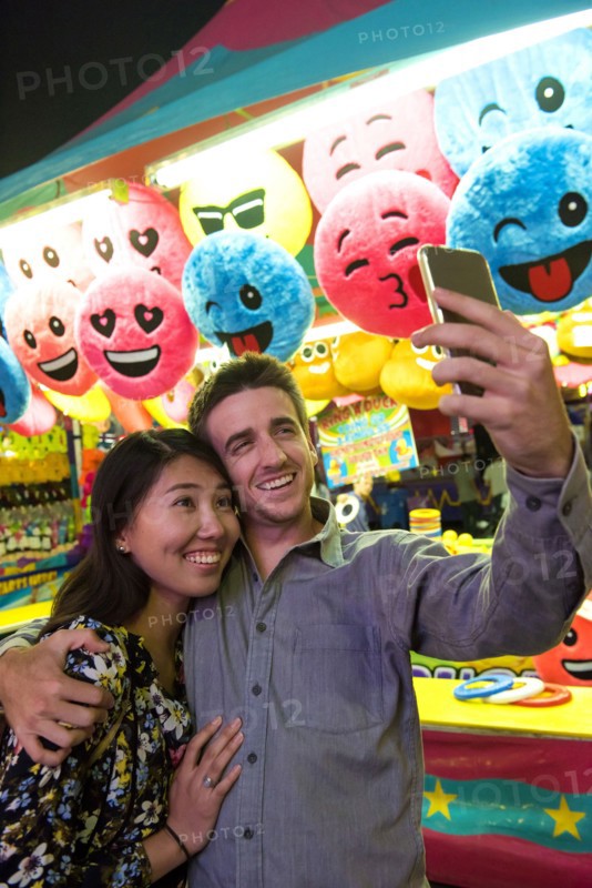 Smiling couple posing for cell phone selfie in amusement park
