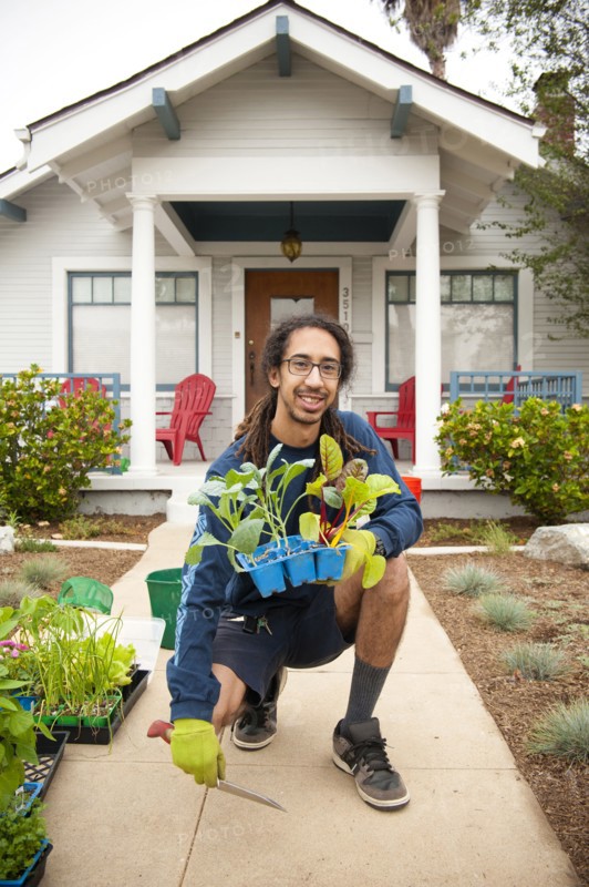 Portrait of smiling Black man holding tray of plants near house
