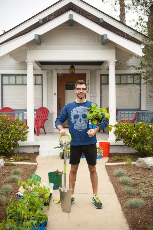 Portrait of smiling Hispanic man holding shovel and plants near house
