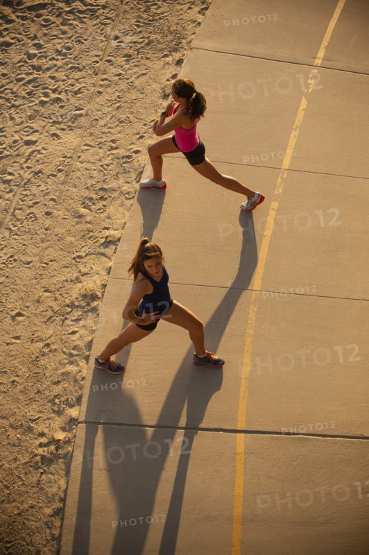 Mixed Race mother and daughter stretching on path at beach