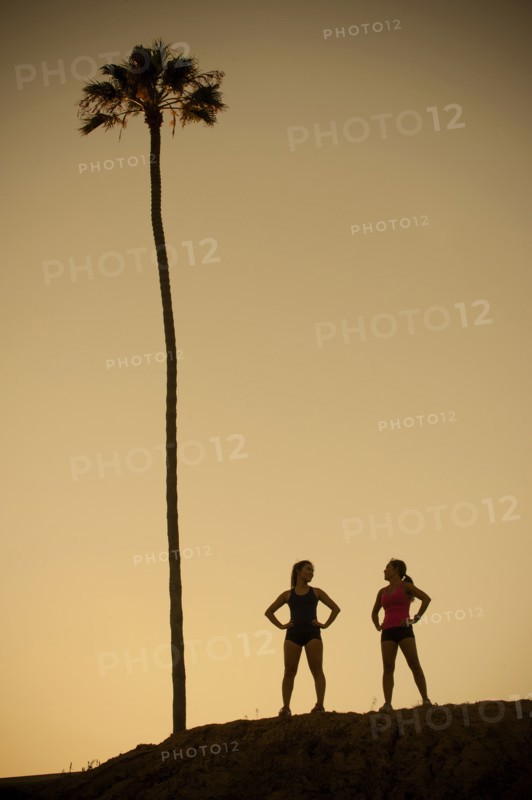Mixed Race mother and daughter standing near palm tree