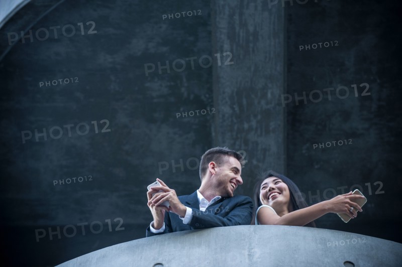 Low angle view of couple on balcony texting on cell phones