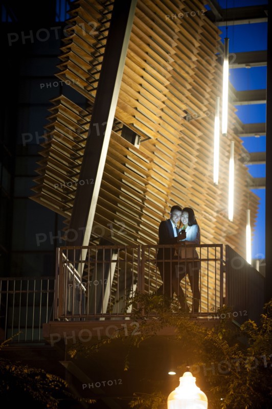 Couple standing on balcony posing for cell phone selfie at night