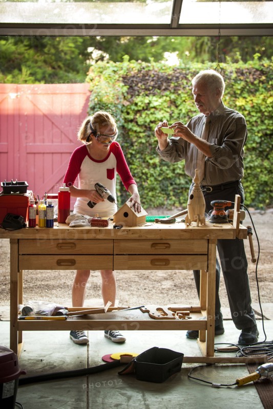 Grandfather photographing granddaughter building birdhouse in garage