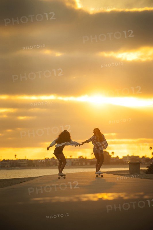 Girl holding hands while skateboarding on waterfront at sunset